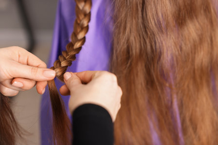 Hairstylist braiding girl's hair in salon, closeupの写真素材