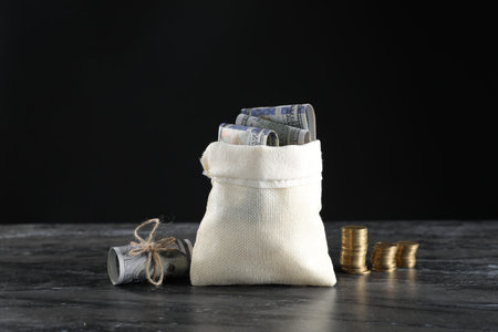 Burlap sack with dollar banknotes and stacked coins on grey table