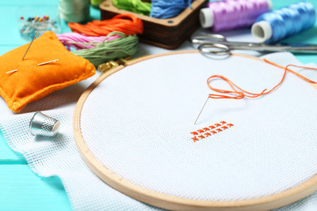 Embroidery. Canvas with cross stitches and supplies on turquoise wooden table, closeupの写真素材
