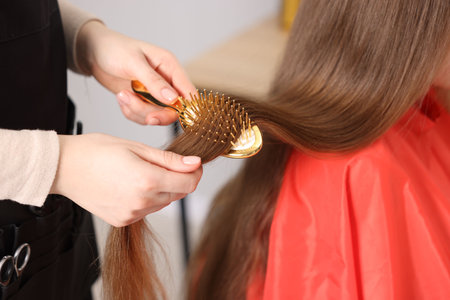 Hairdresser brushing girl's hair in salon, closeupの写真素材