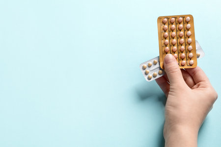 Woman holding blisters of contraceptive pills on light blue background, closeup. Space for textの写真素材