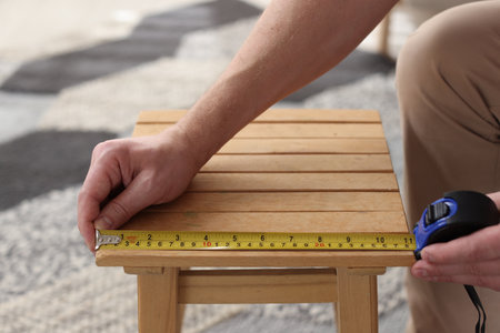 Man measuring wooden stool with tape indoors, closeupの写真素材