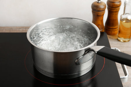 Saucepan with boiling water and stove on wooden table against white background, closeupの写真素材