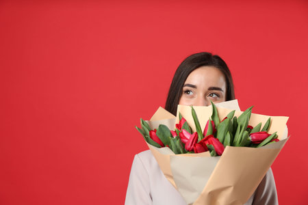 Happy woman with tulip flowers bouquet on red background, space for text. 8th of March celebrationの写真素材