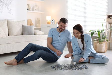 Happy couple solving puzzle together on floor indoorsの写真素材