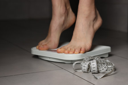 Woman on scales and measuring tape indoors, closeup.の写真素材