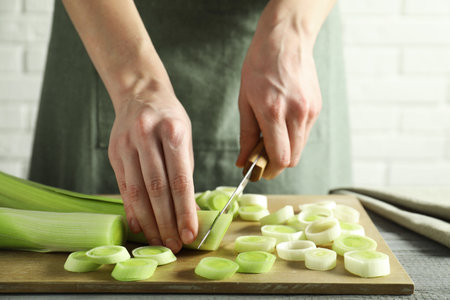 Woman cutting fresh leek at gray wooden table, closeupの写真素材