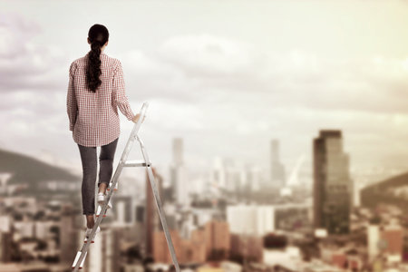 Woman on metal step ladder against blurred cityscape, back view. Space for textの写真素材
