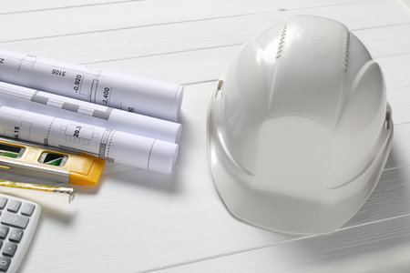 Different technical drawings, hard hat, calculator, building level and measuring tape on white...