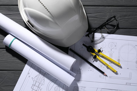 Different engineering drawings, hard hat, glasses, pencil and divider on gray wooden table, flat layの写真素材