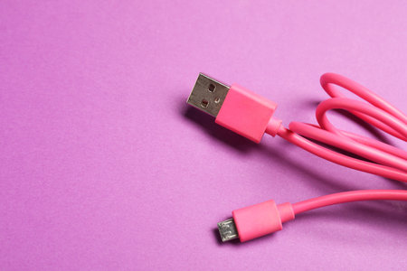 Pink USB charge cable on purple background, closeup. Space for text