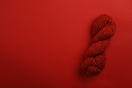 Soft woolen yarn on red background, top view. Space for text