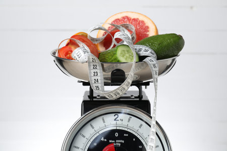 Kitchen scales with products and measuring tape on white background, closeup