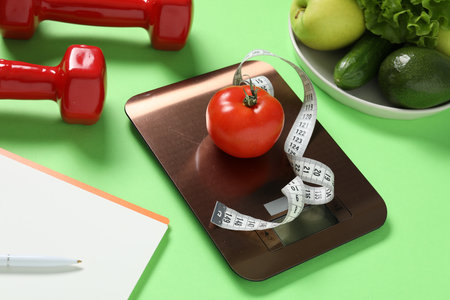 Electronic kitchen scale, measuring tape, dumbbells, notepad and products on light green background, closeup. Calories controlの写真素材