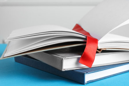 Book with red ribbon bookmark and colorful ones on light blue background, closeupの写真素材