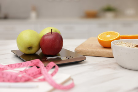 Kitchen scales, fruits, oatmeal and measuring tape on white marble table indoors, closeupの写真素材