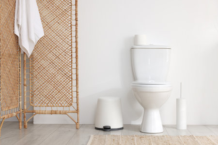 Toilet, brush and necessities near white wall in bathroomの写真素材