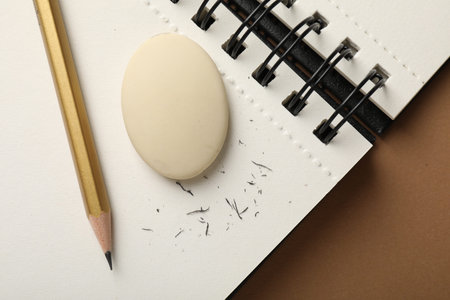 Eraser, pencil, scraps and notebook on brown background, top view