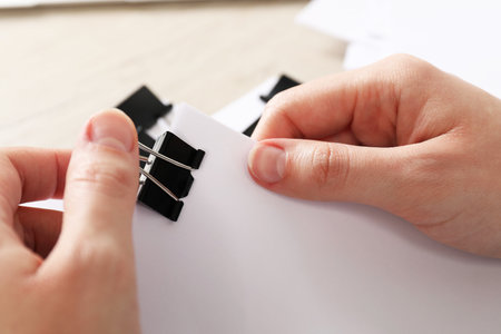 Woman attaching sheets of paper with metal binder clip at table, closeupの写真素材