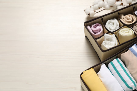 Organizers with folded clothes and cotton branch on light wooden table, above view. Space for textの写真素材