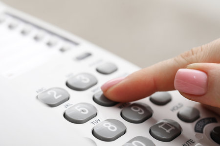 Woman dialing number on telephone against blurred gray background, closeupの写真素材