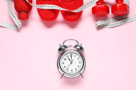 Alarm clock, sneakers, dumbbells, measuring tape and water bottle on pink background, flat layの写真素材