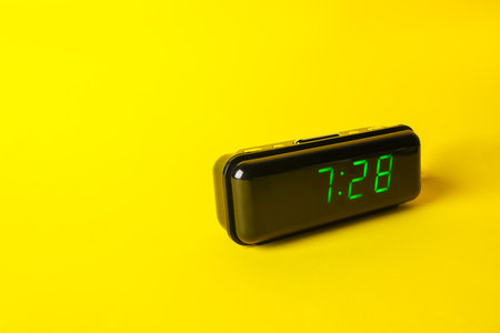 Digital alarm clock showing 7:28 o'clock on yellow background, space for textの写真素材
