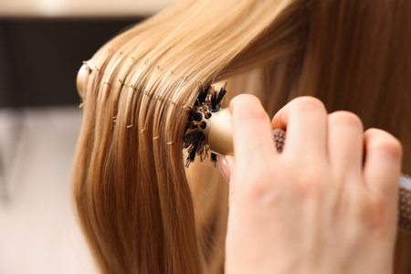 Hairdresser styling client's hair with round brush in salon, closeupの写真素材