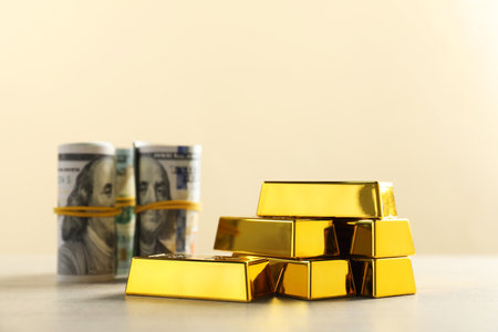 Shiny gold bars and money on beige background, selective focus. Space for textの写真素材