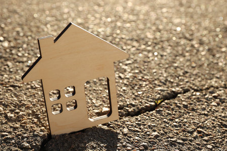 Wooden house model on cracked asphalt demonstrating earthquake disasterの写真素材