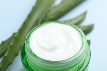 Moisturizing cream with extract of aloe vera and cut leaves on light blue background, closeupの写真素材