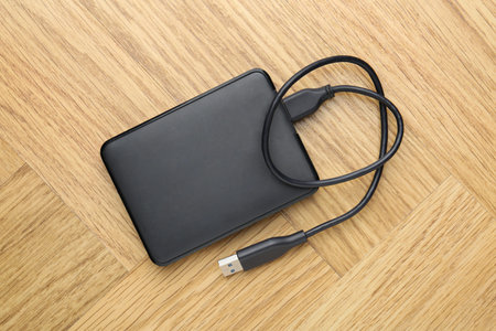 External hard drive with USB cable on light wooden table, top viewの写真素材