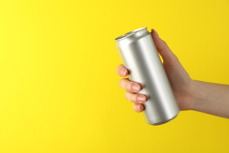 Hand with tin can on yellow background, closeup. Space for textの写真素材