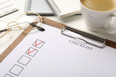 Checklist with marked checkboxes, stationery, glasses and coffee on white table, closeupの写真素材