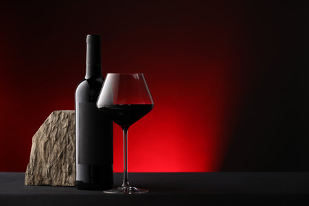 Bottle of wine, wineglass and rock on black table against dark red background, space for textの写真素材