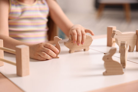 Motor skills development. Little girl playing with wooden animals at table indoors, closeupの写真素材