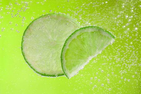 Soda water with lime slices against light green background, closeup
