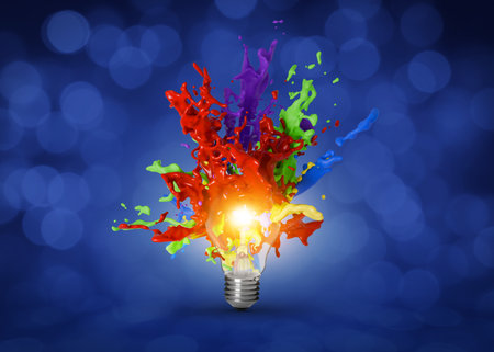 Idea concept. Splashes of bright paints flying out of glowing light bulb on dark blue background with blurred lightsの写真素材