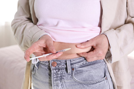 Woman making insulin injection into her belly indoors, closeup. Diabetes