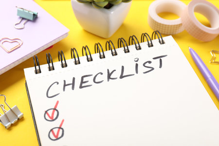 Checklist, plant and stationery on yellow background, closeup