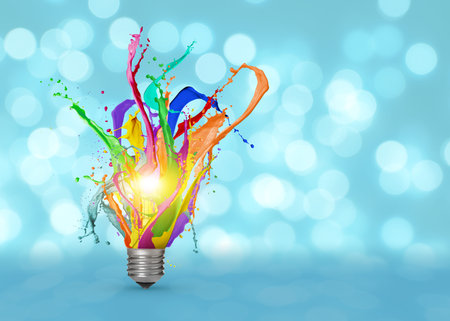 Idea concept. Splashes of bright paints flying out of glowing light bulb on light blue background with blurred lightsの写真素材