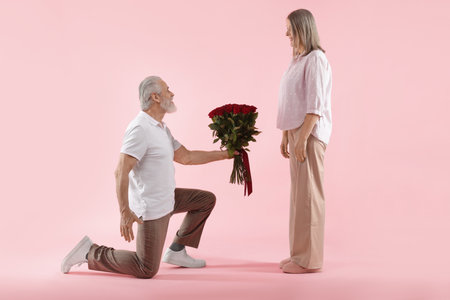 Man presenting bouquet of red roses to his happy wife on pink backgroundの写真素材