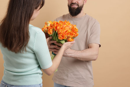 Man presenting bouquet of beautiful tulips to his beloved woman on beige background, closeupの写真素材