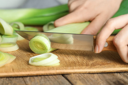 Woman cutting fresh leek at wooden table, closeupの写真素材