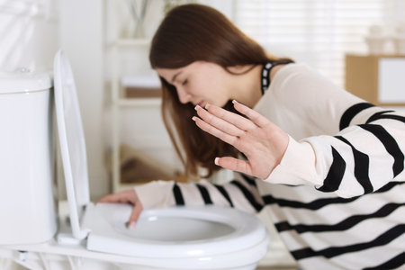Teenage girl suffering from nausea over toilet bowl showing stop gesture indoors, selective focus. Bulimiaの写真素材