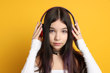 Teenage girl wearing stylish clothes and headphones on orange background. Makeup in anime styleの写真素材