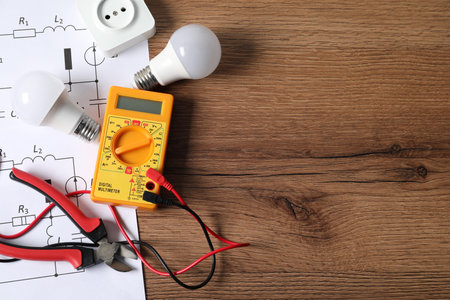 Different electrical tools and circuit diagrams on wooden table, flat lay. Space for text