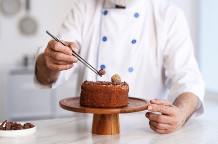Elderly pastry chef decorating cake at table in kitchen, closeupの写真素材
