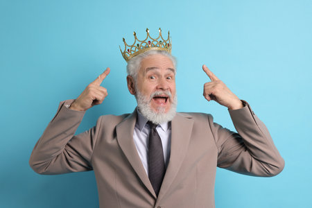 Senior man pointing at luxury crown on light blue backgroundの写真素材