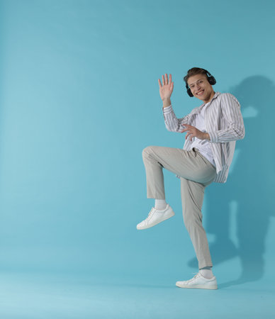 Happy man in headphones dancing on light blue background. Space for textの写真素材
